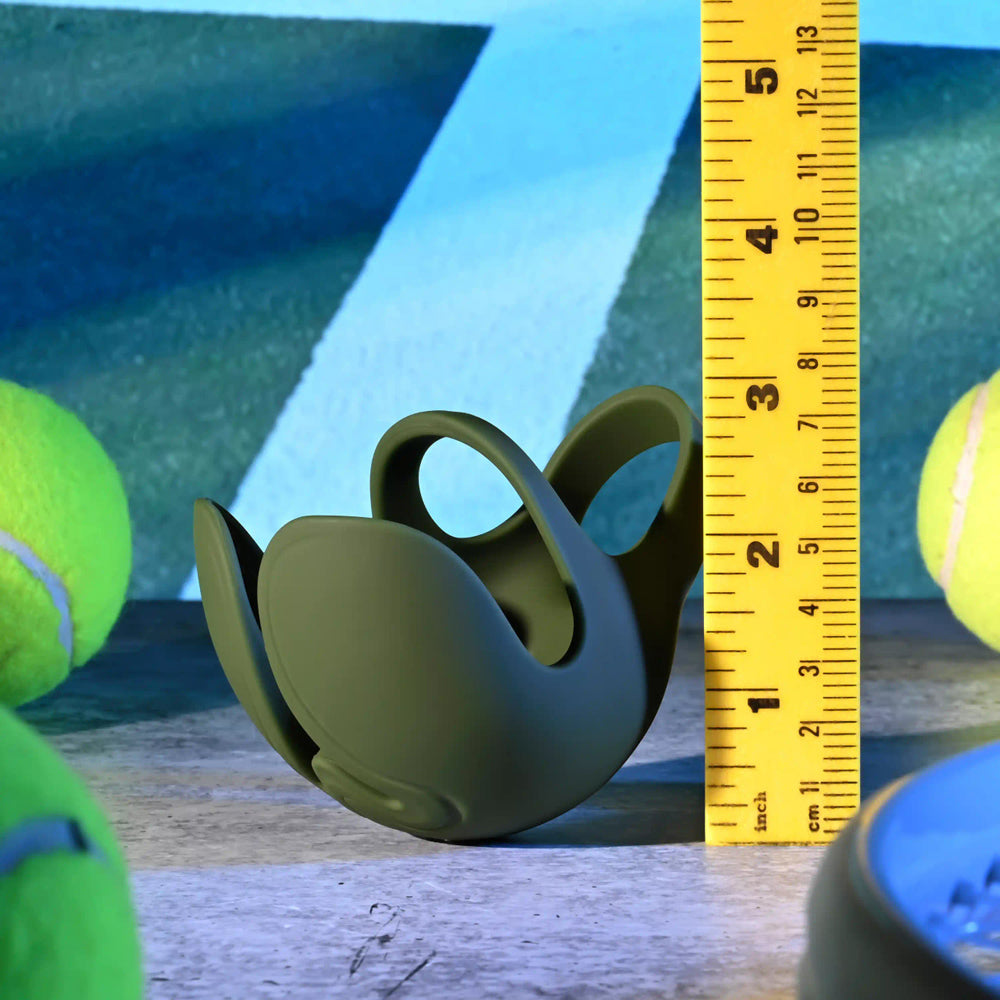 A green vibrating silicone ball ring with a textured shield sits next to a ruler and tennis balls.