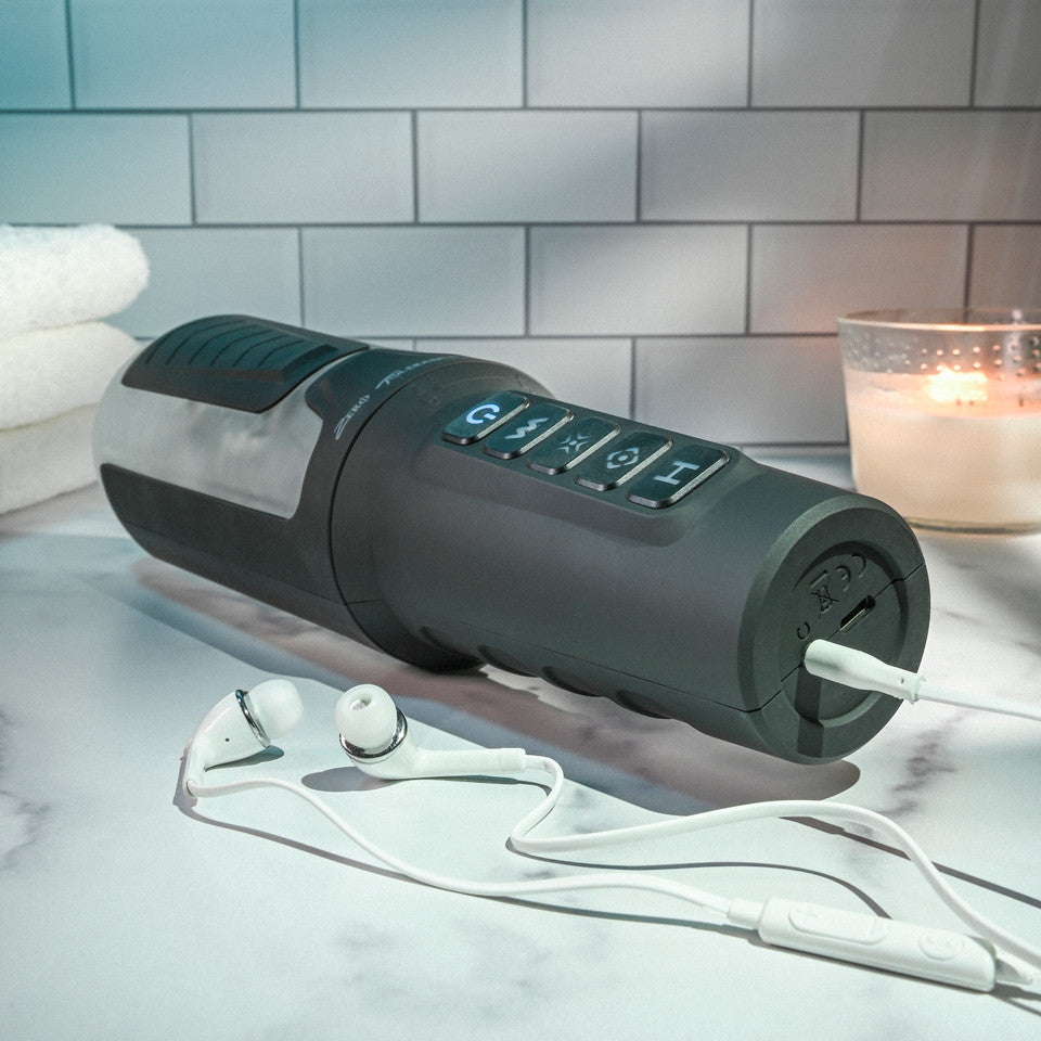A dark gray vibrating stroker with buttons and earbuds plugged in.