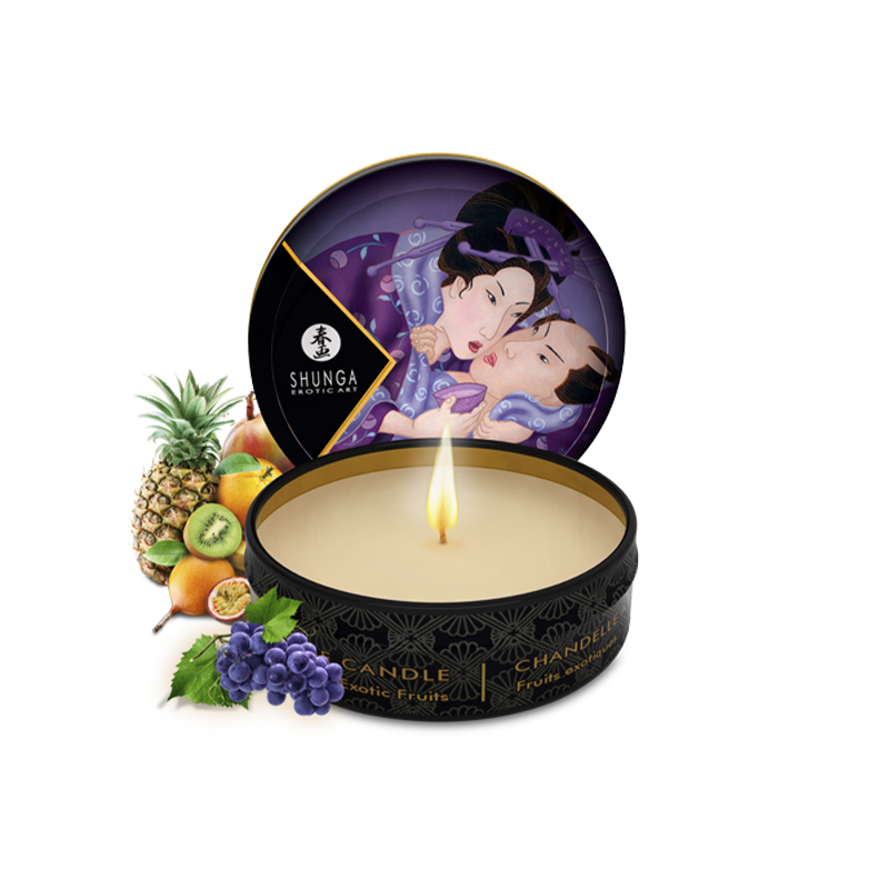 A Shunga Exotic Fruits massage candle with fruit and a lit wick.