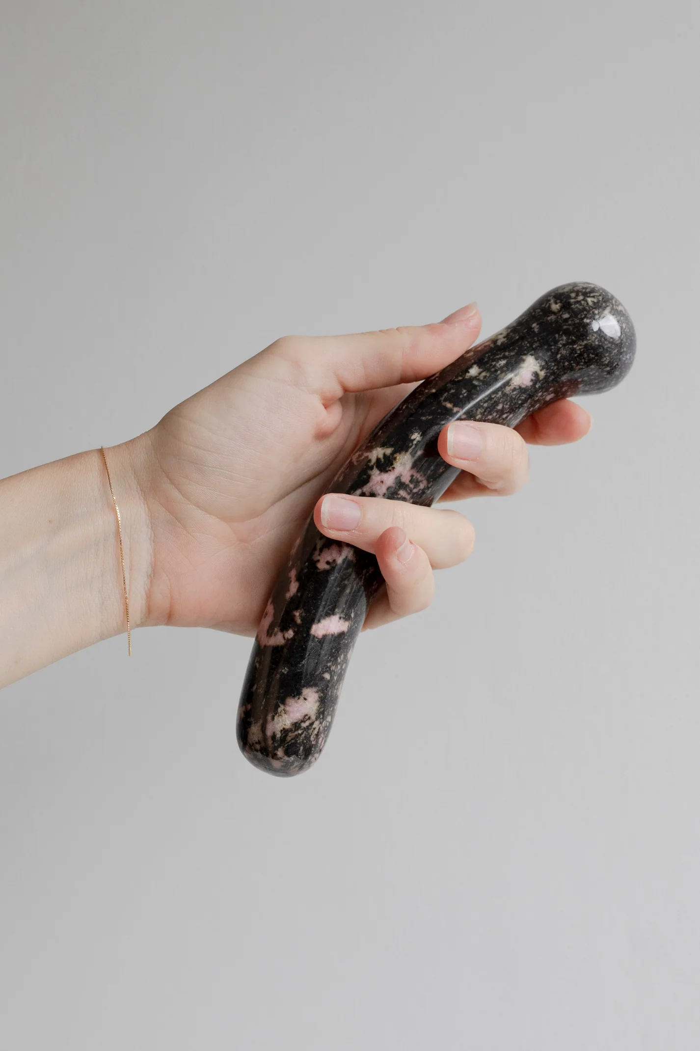 A hand holds a dark, patterned crystal wand with pink inclusions.