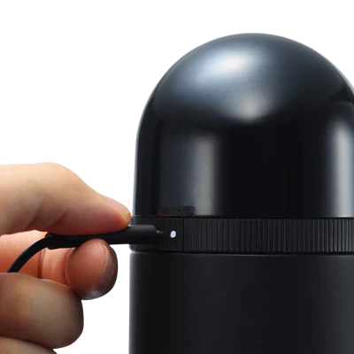 A hand inserts a cable into a black vacuum suction device with a ribbed band and a dome top.