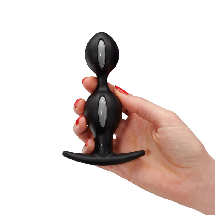 A black weighted anal plug with two silver buttons and a flared base held by a hand.