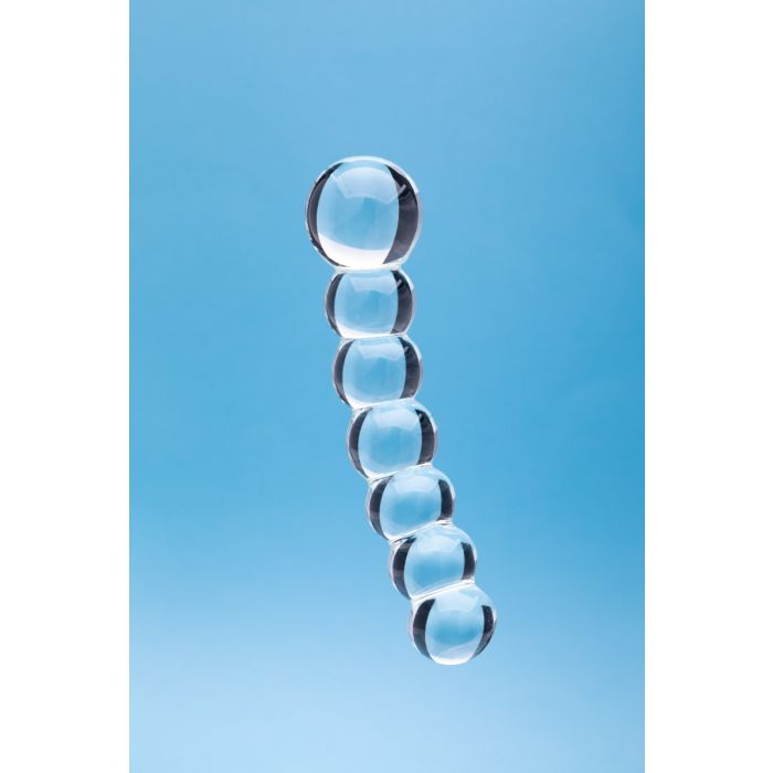 Clear glass dildo with seven connected spheres against a blue background.