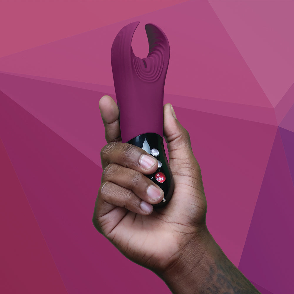 A hand holds a garnet-colored textured stroker and vibrator.