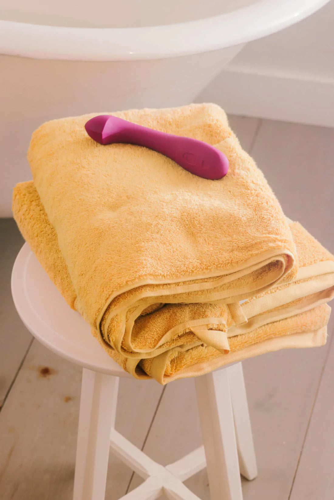 A plum-colored G-spot vibrator rests on folded yellow towels.