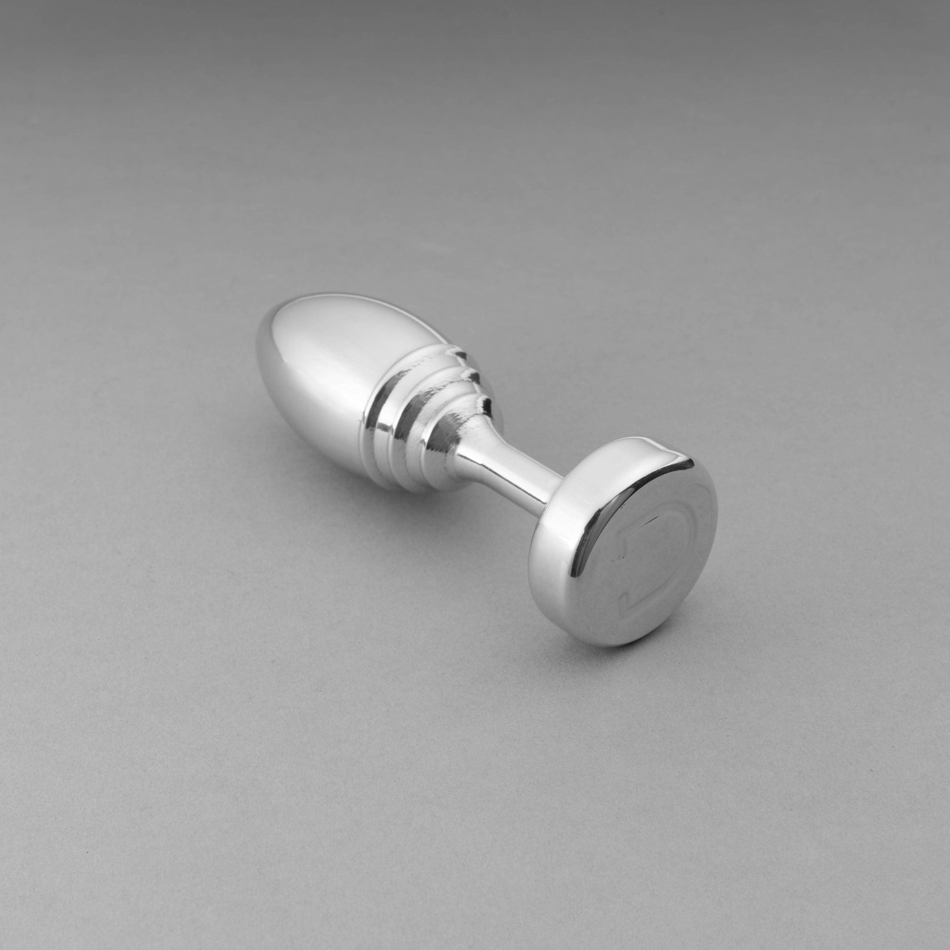 A weighted aluminum butt plug with ribbed detailing and a flat base.