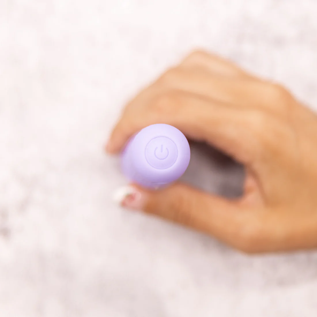A hand holds a small purple vibrator with a power button.