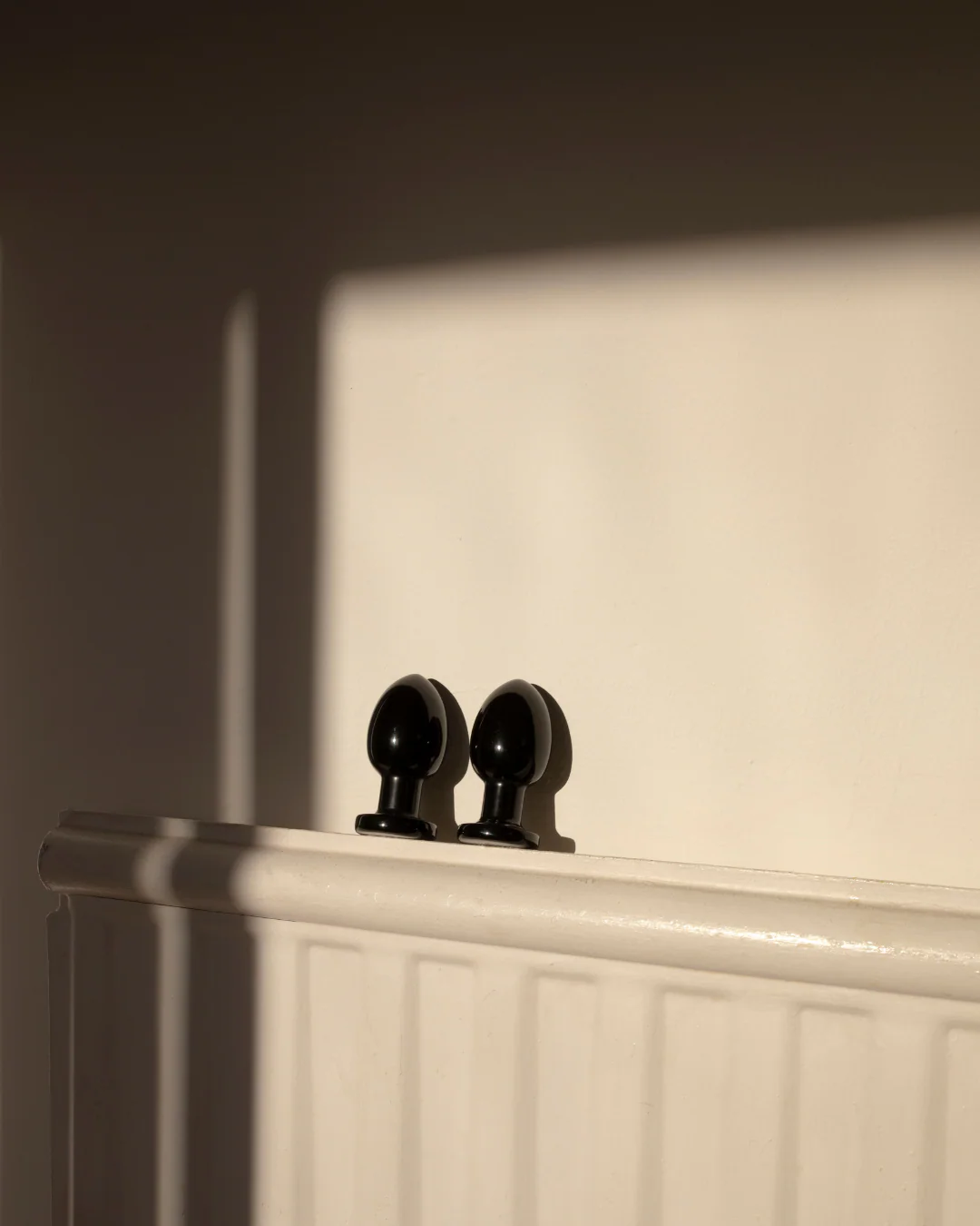 Two black obsidian anal wands rest on a white surface.