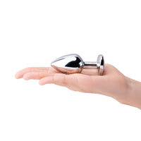 A silver metal anal plug with a pink gem base rests on a hand.