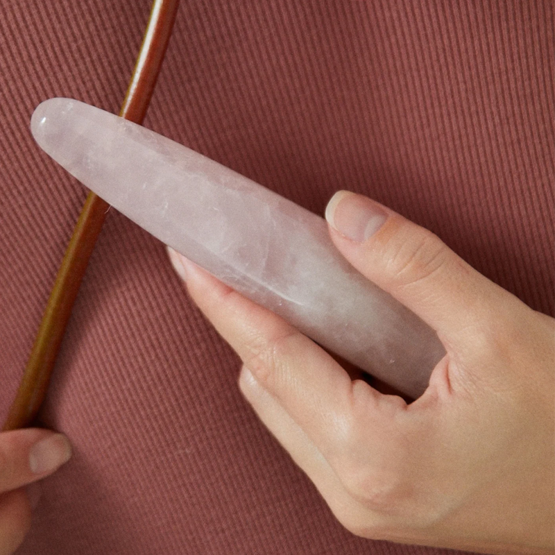 A slim, pink rose quartz crystal wand held in a hand.