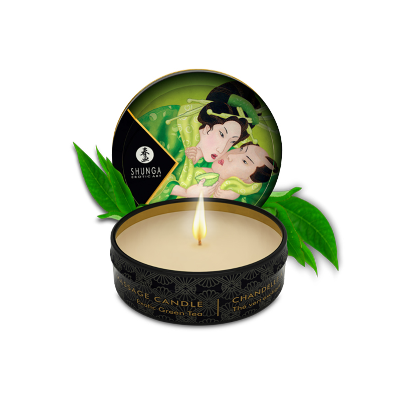 Shunga Exotic Green Tea massage candle with a lit wick and decorative lid.