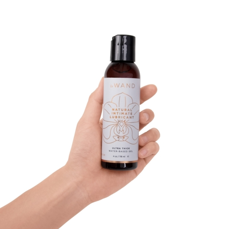 A hand holds a bottle of Le Wand Natural Intimate Lubricant.