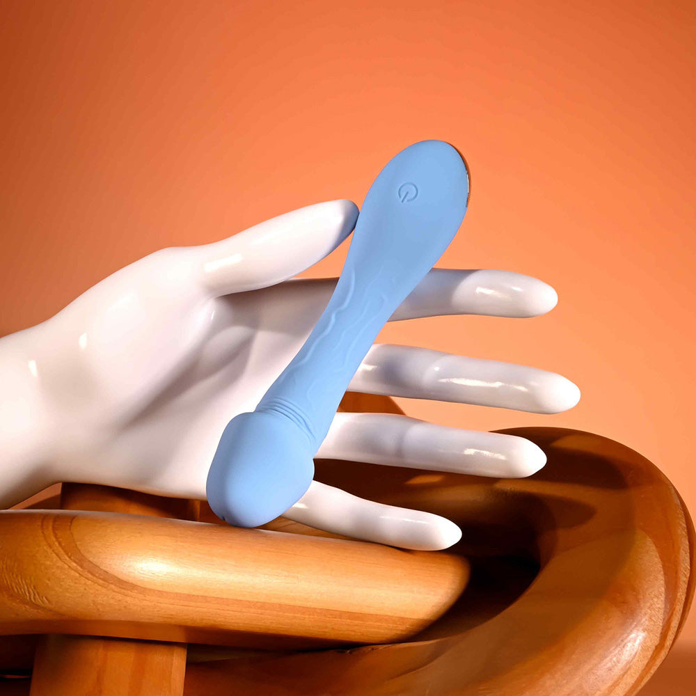 A blue silicone vibrator with a curved head rests on a mannequin hand.