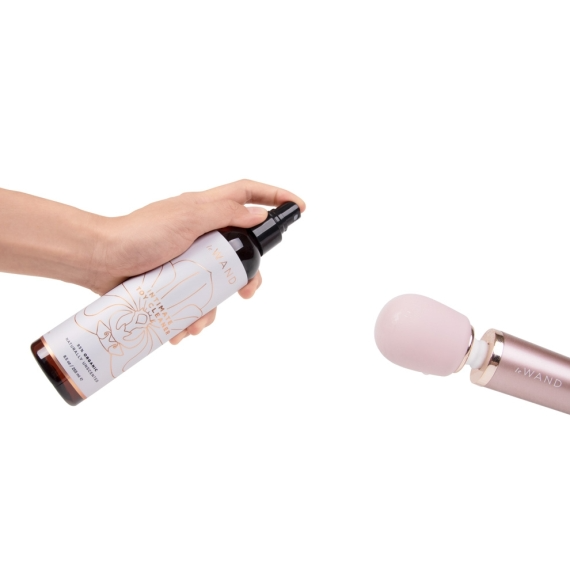 A hand holds a bottle of Le Wand intimate toy cleaner next to a pink wand.