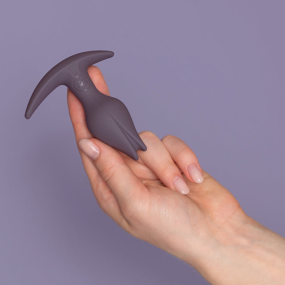 A grey anal plug with an asymmetrical base held in a hand.
