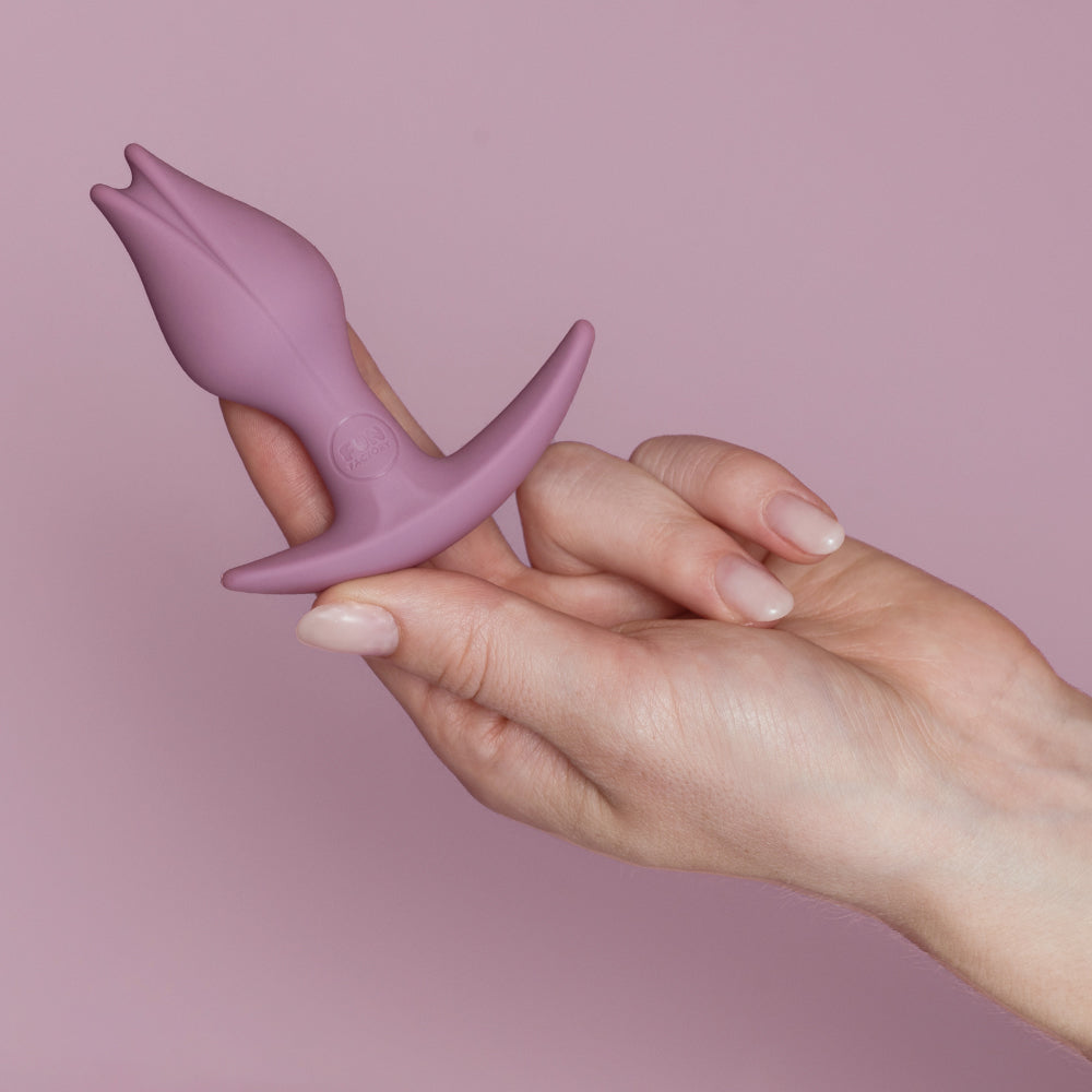 A purple Bootie Slim anal plug with an asymmetrical base held by a hand.