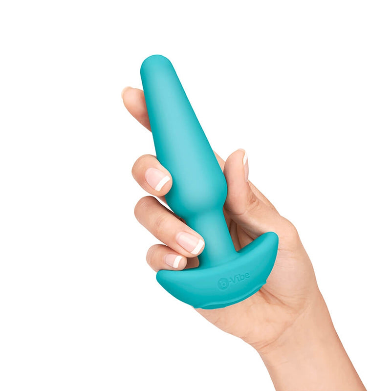 A hand holds a teal silicone butt plug with a flared base.