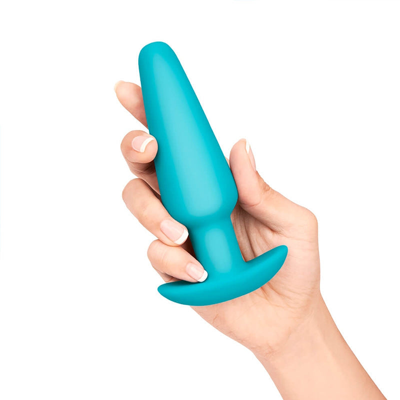 A teal silicone butt plug with a flared base is held in a hand.