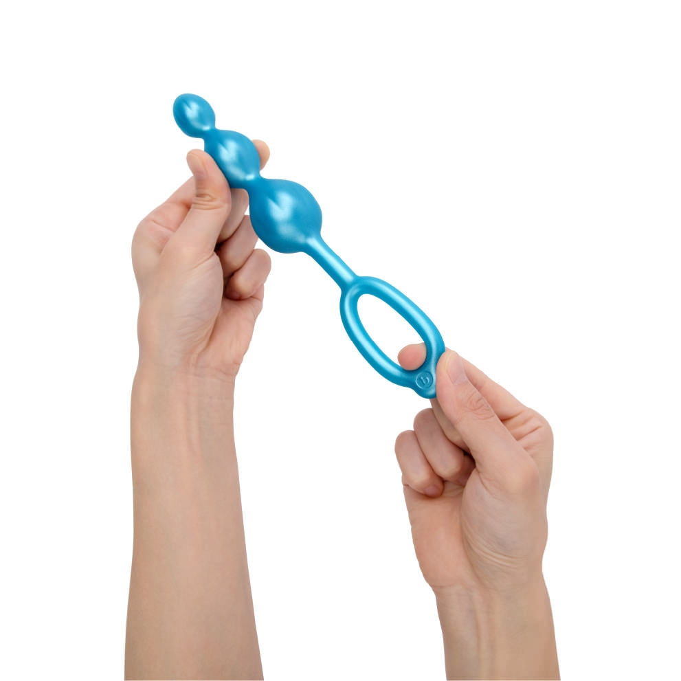 A blue beaded anal training plug with a loop handle is held by two hands.
