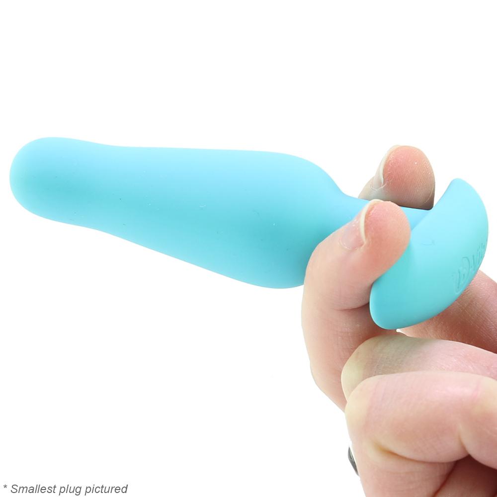 A hand holds a small, teal silicone butt plug.