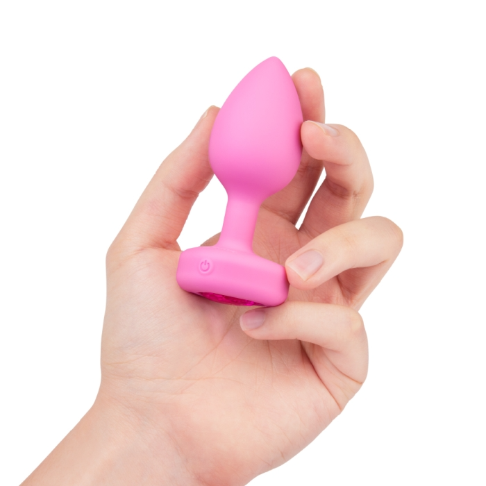 A pink silicone vibrating anal plug with a power button is held in a hand.