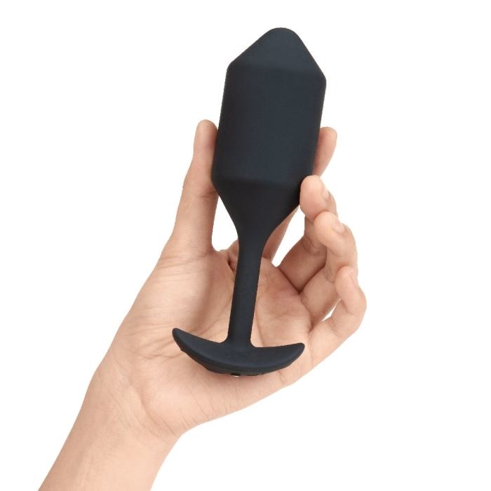 A hand holds a black silicone vibrating snug plug with a flared base.