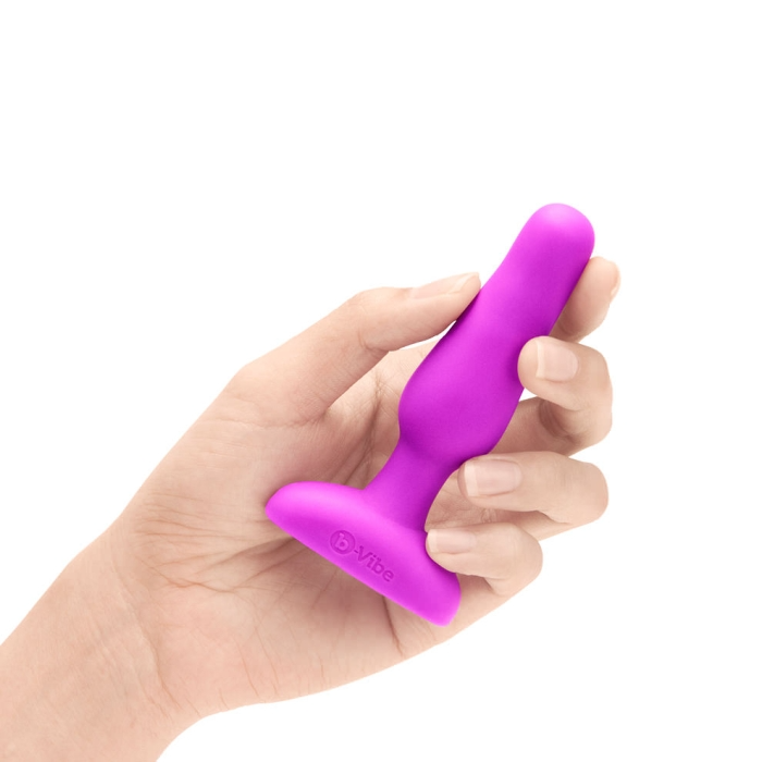 A fuchsia vibrating anal plug with a flared base is held in a hand.