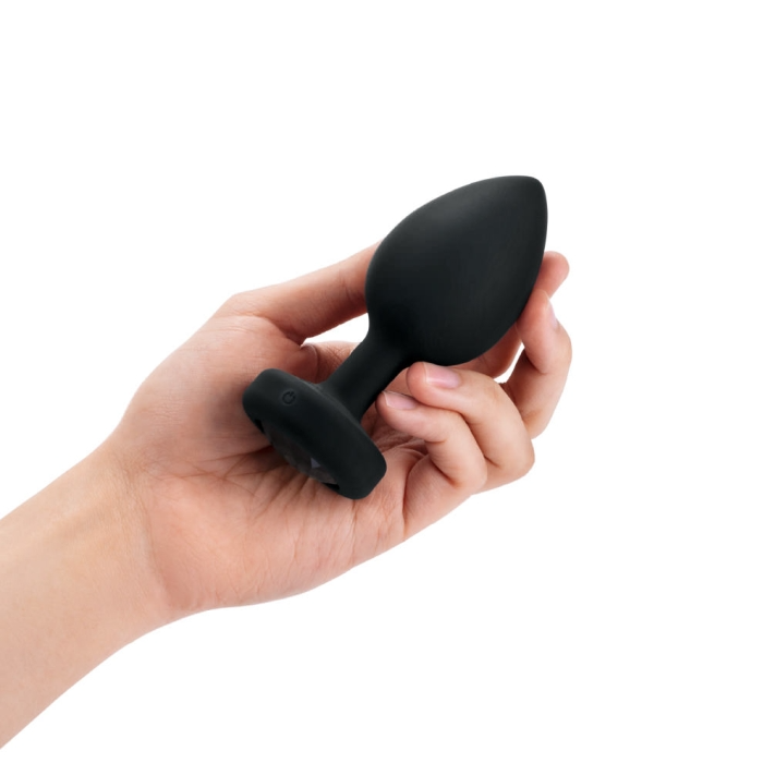 A black silicone vibrating anal plug with a flared base is held in a hand.