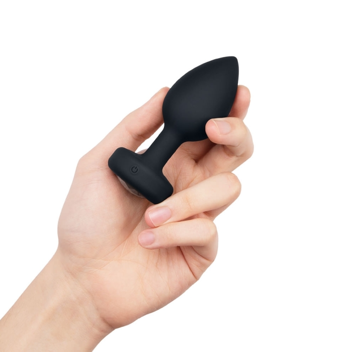 A hand holds a black vibrating anal plug with a power button.