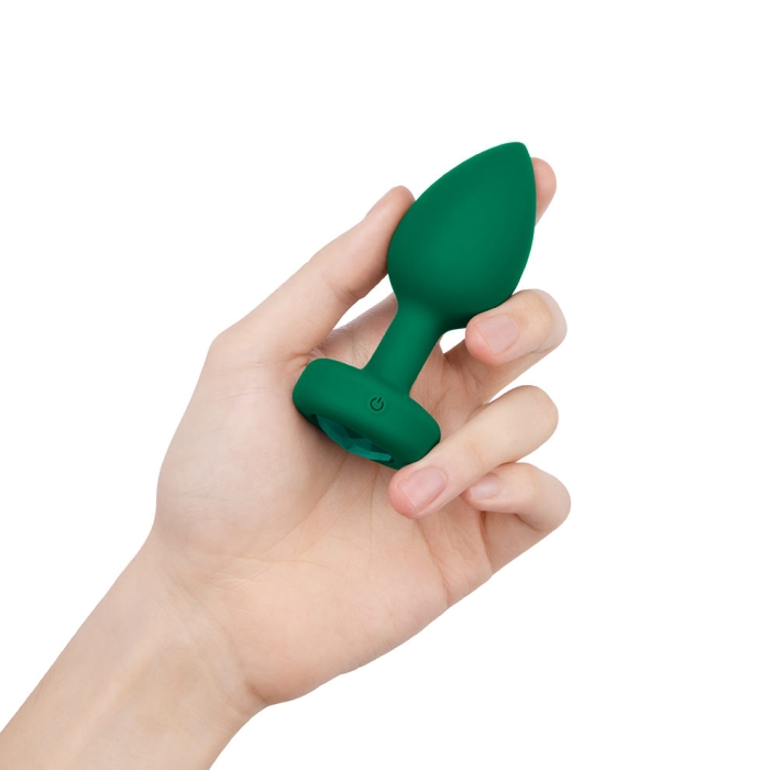 A hand holds a green vibrating anal plug with a jewel accent.