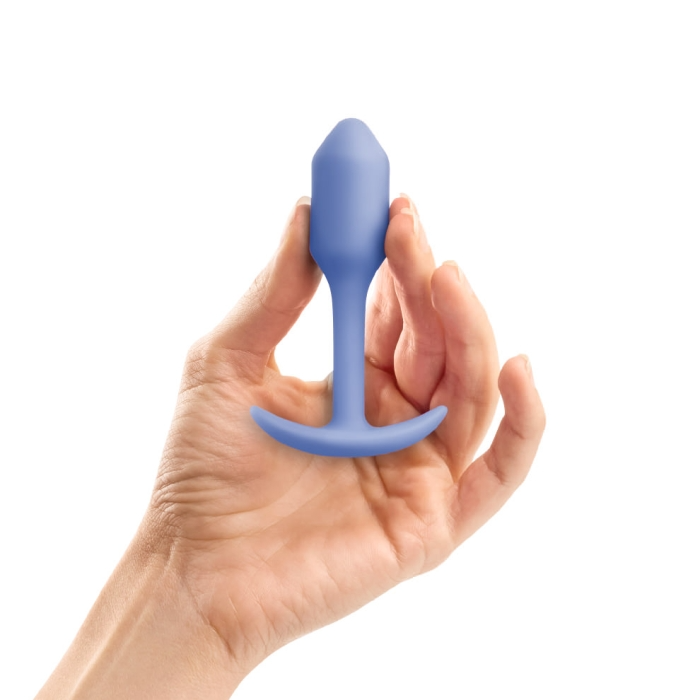 A hand holds a violet weighted silicone anal plug.