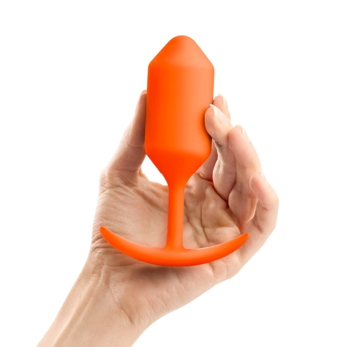 A hand holds an orange silicone anal plug with a flared base.