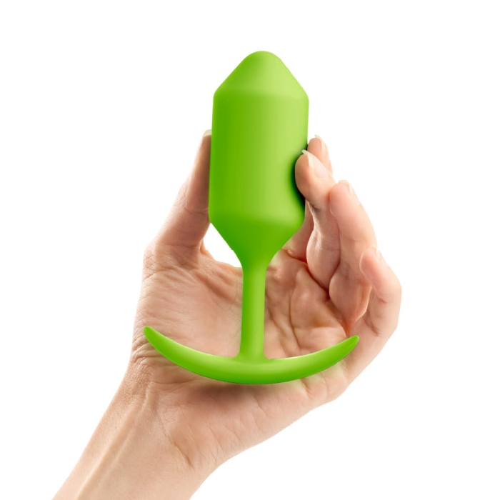 A hand holds a lime green weighted silicone anal plug with a flared base.