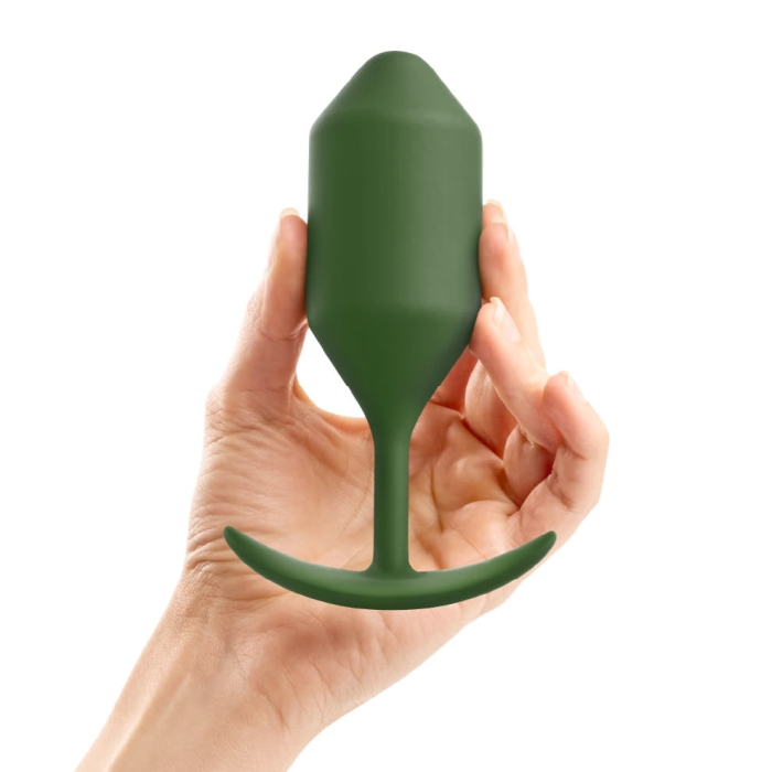 A hand holds a weighted army green silicone anal plug with a flared base.