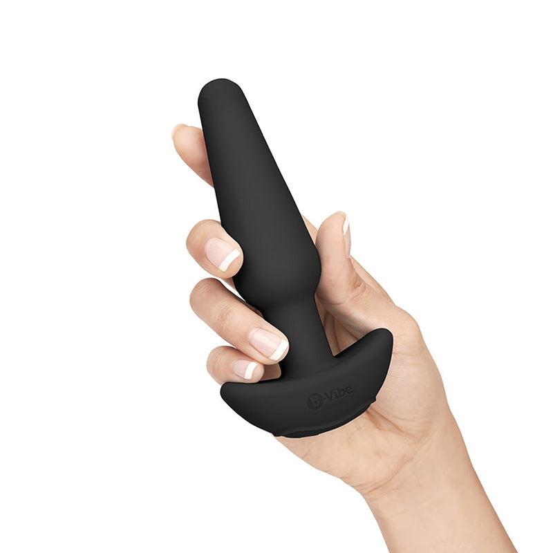 A black silicone butt plug with a flared base is held by a hand.