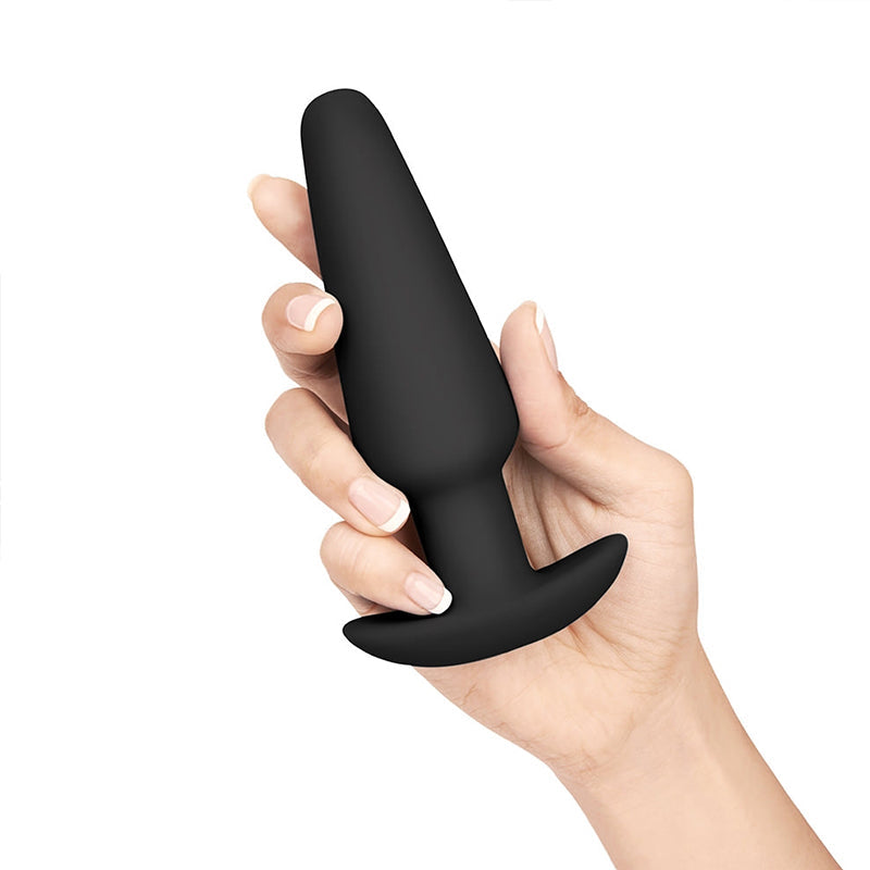 A black silicone butt plug with a flared base is held in a hand.