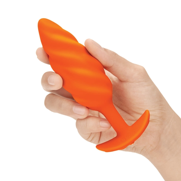 Orange silicone anal plug with a swirl texture held in a hand.