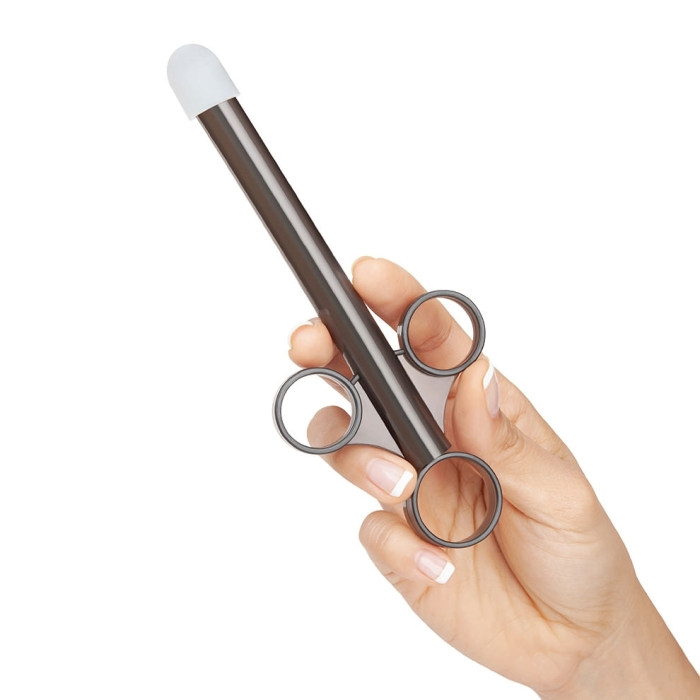 A hand holds a dark brown lube applicator with a white tip and finger loops.