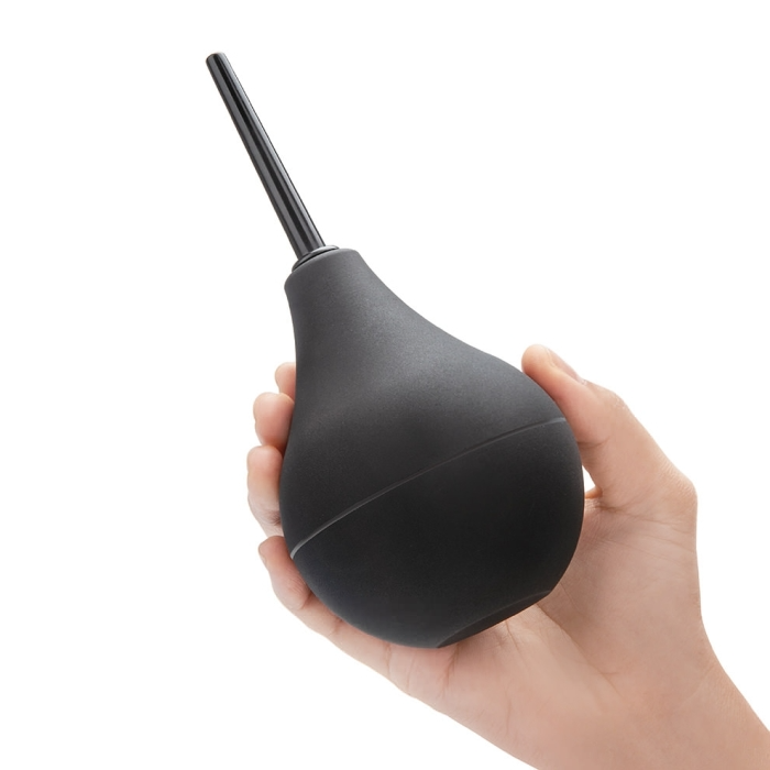 A hand holds a black enema bulb with a pointed tip.