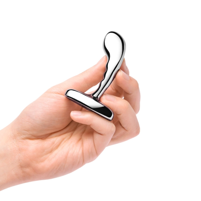 A hand holds a shiny, curved stainless steel prostate plug.