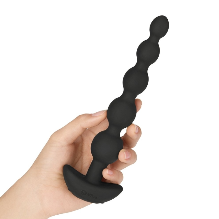 A hand holds black vibrating anal beads with a remote control.