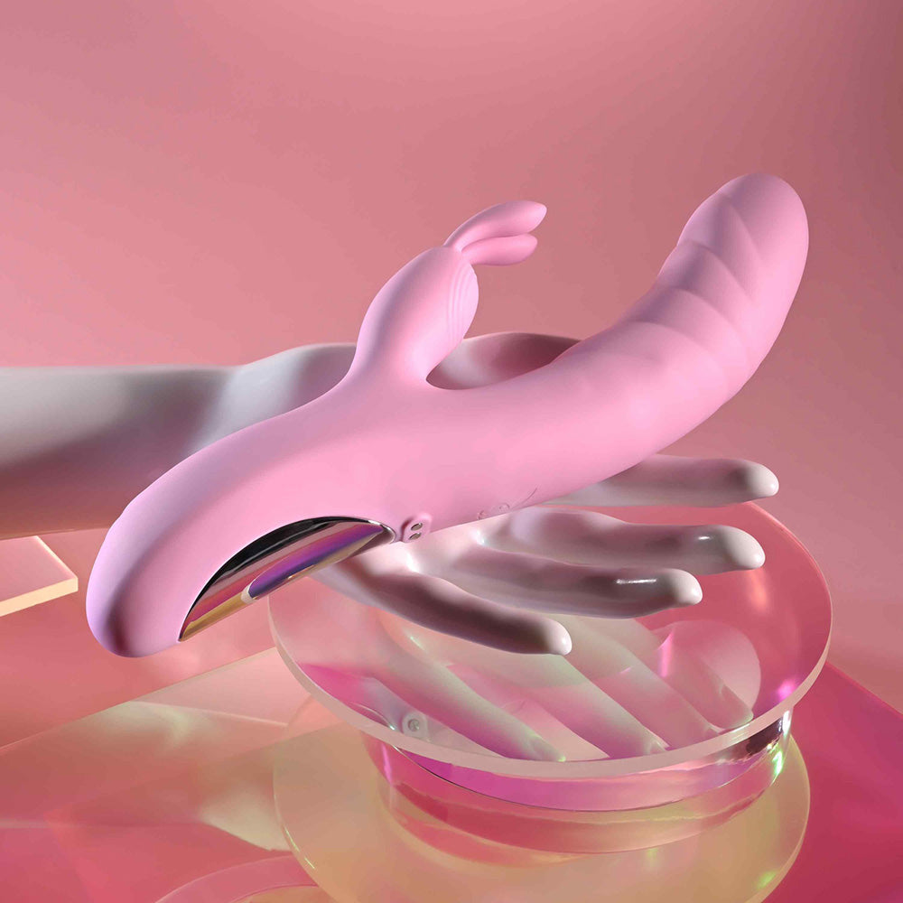 A pink rabbit vibrator with a curved shaft rests on a translucent pink dish.
