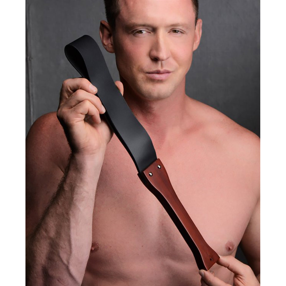 Man holding a wooden slapper with a black PU leather strap.