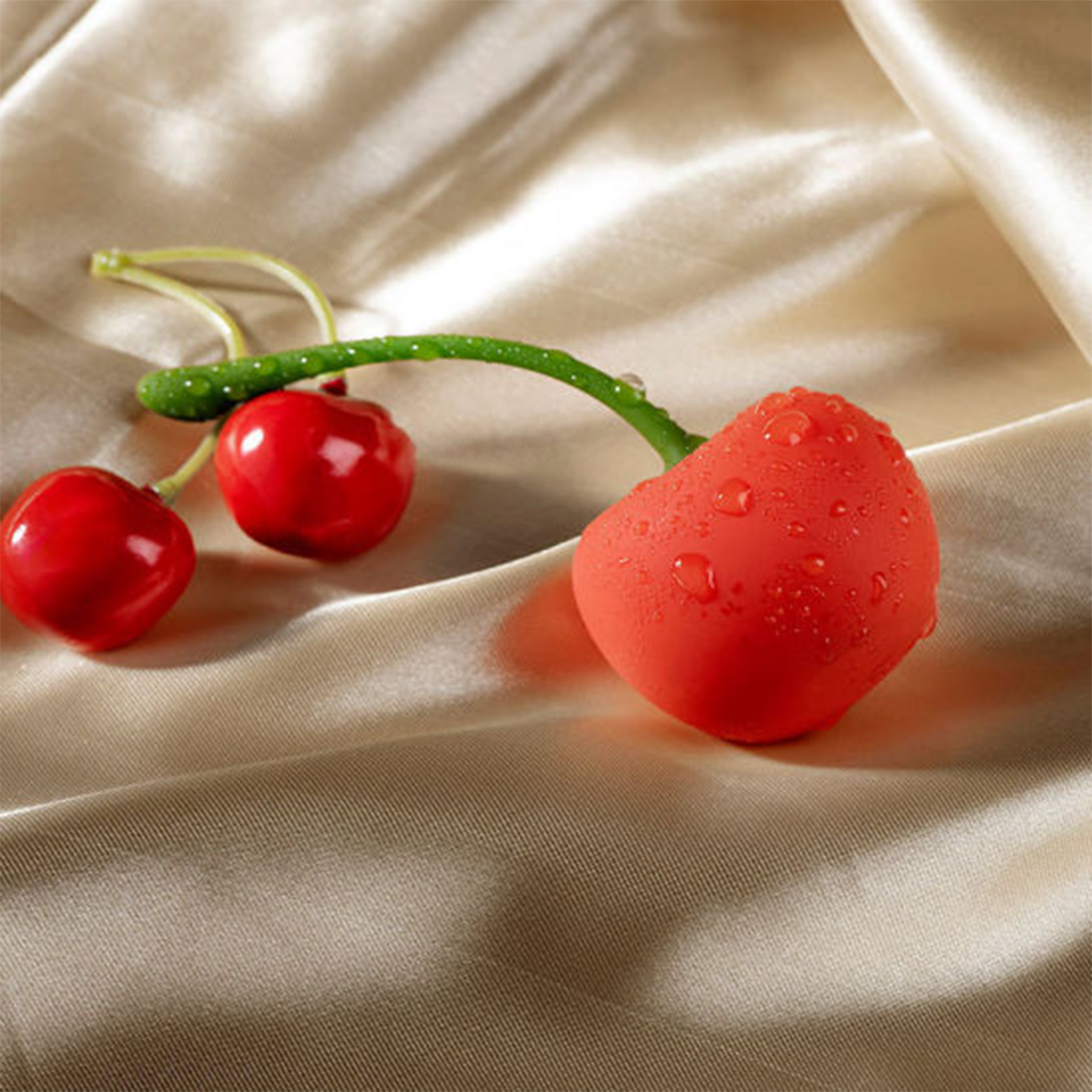 Red cherry-shaped vibrator with water droplets on a satin background.