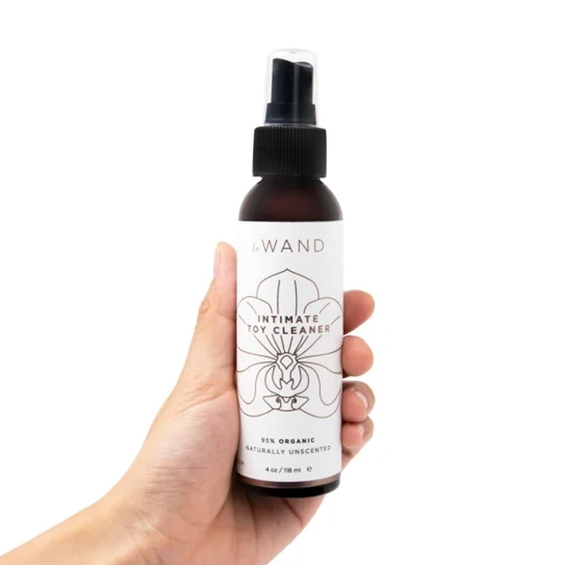 A hand holds a bottle of Le Wand Organic Intimate Toy Cleaner.