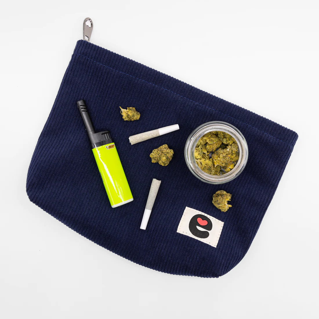 Midnight blue corduroy travel pouch with lighter, joints, and jar of cannabis.