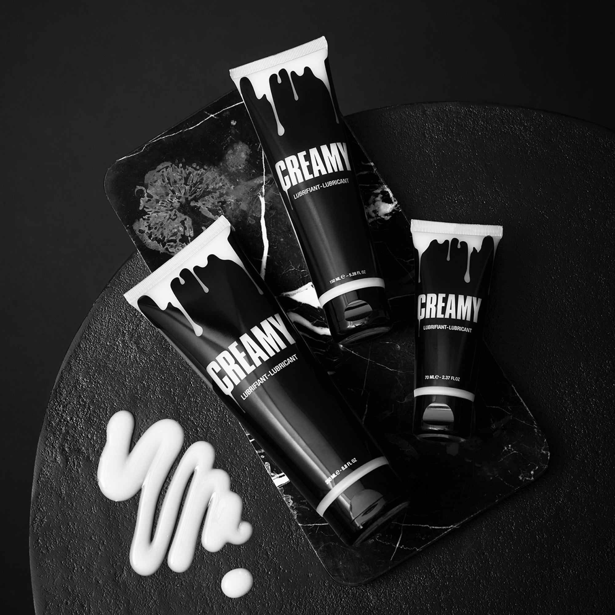 Three tubes of Creamy lubricant with white drips on a black textured surface.