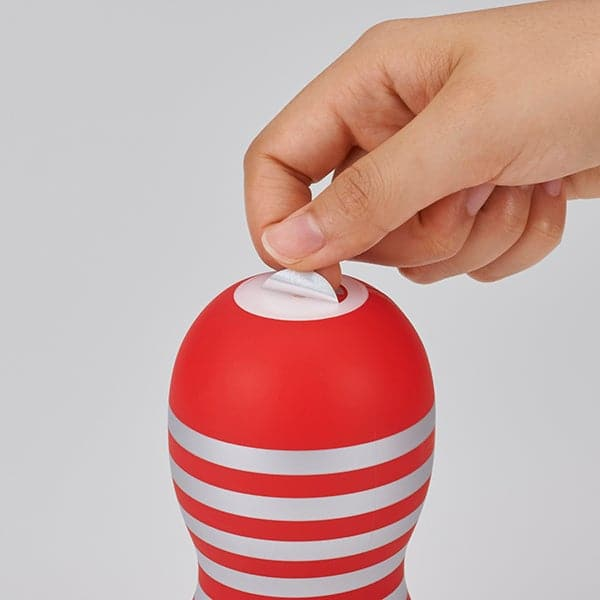 A red and silver striped masturbator cup with a hand peeling off the top seal.