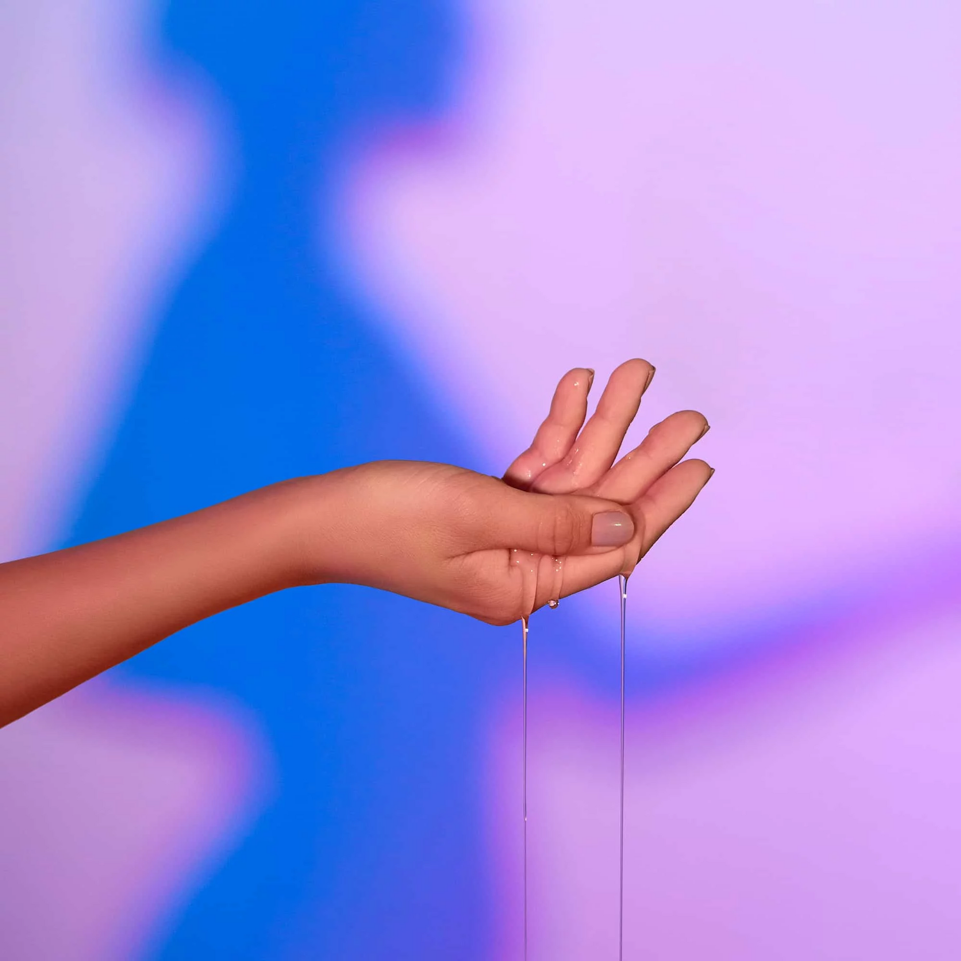 Hand with oil dripping, against a blurred blue and purple background.