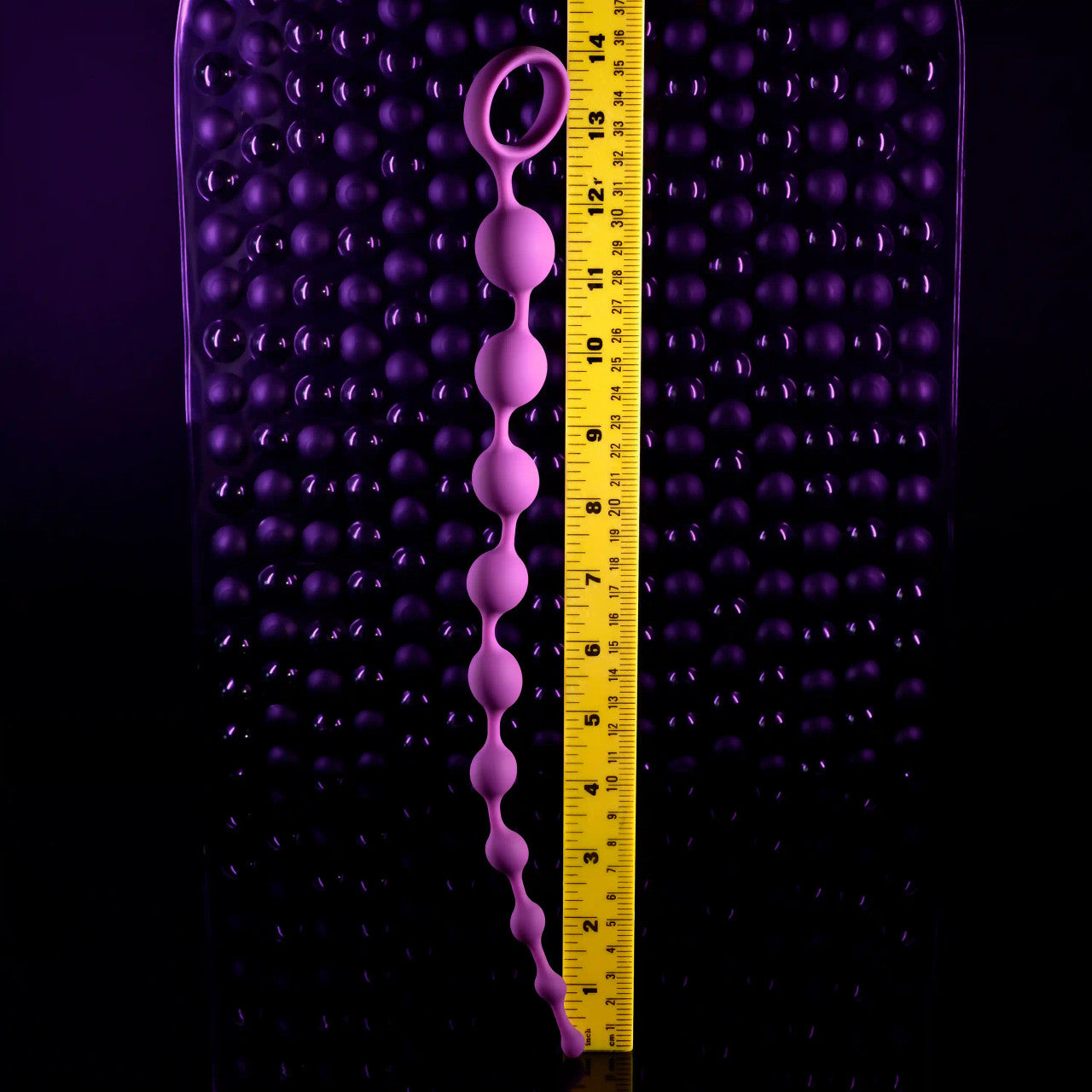 A purple beaded anal string with a retrieval ring is measured against a ruler.